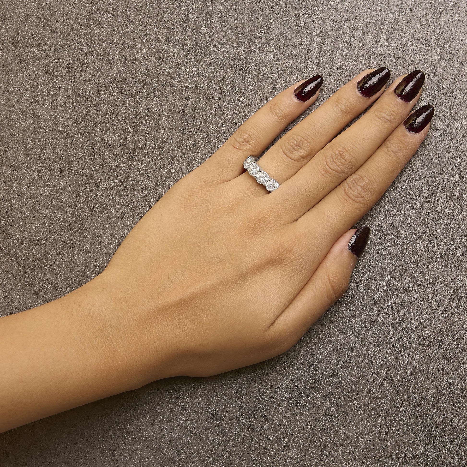 White metal ring with six round white gemstones in shared prong setting, shown worn on a model's hand, angled top view.