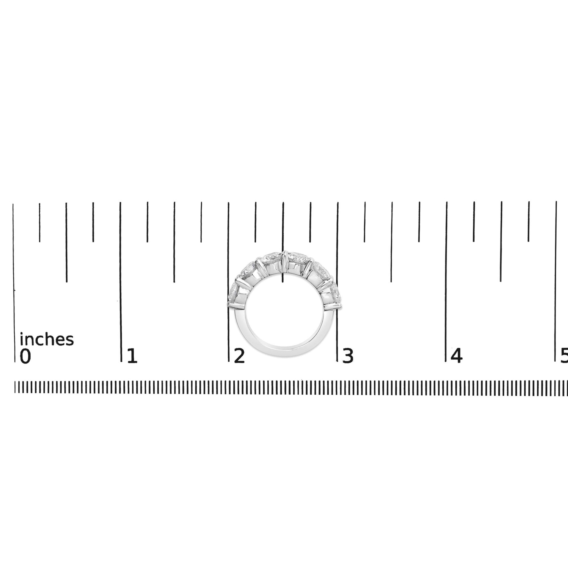 White metal ring with six round white gemstones in shared prong setting, shown resting flat on a ruler scale, top-down view.