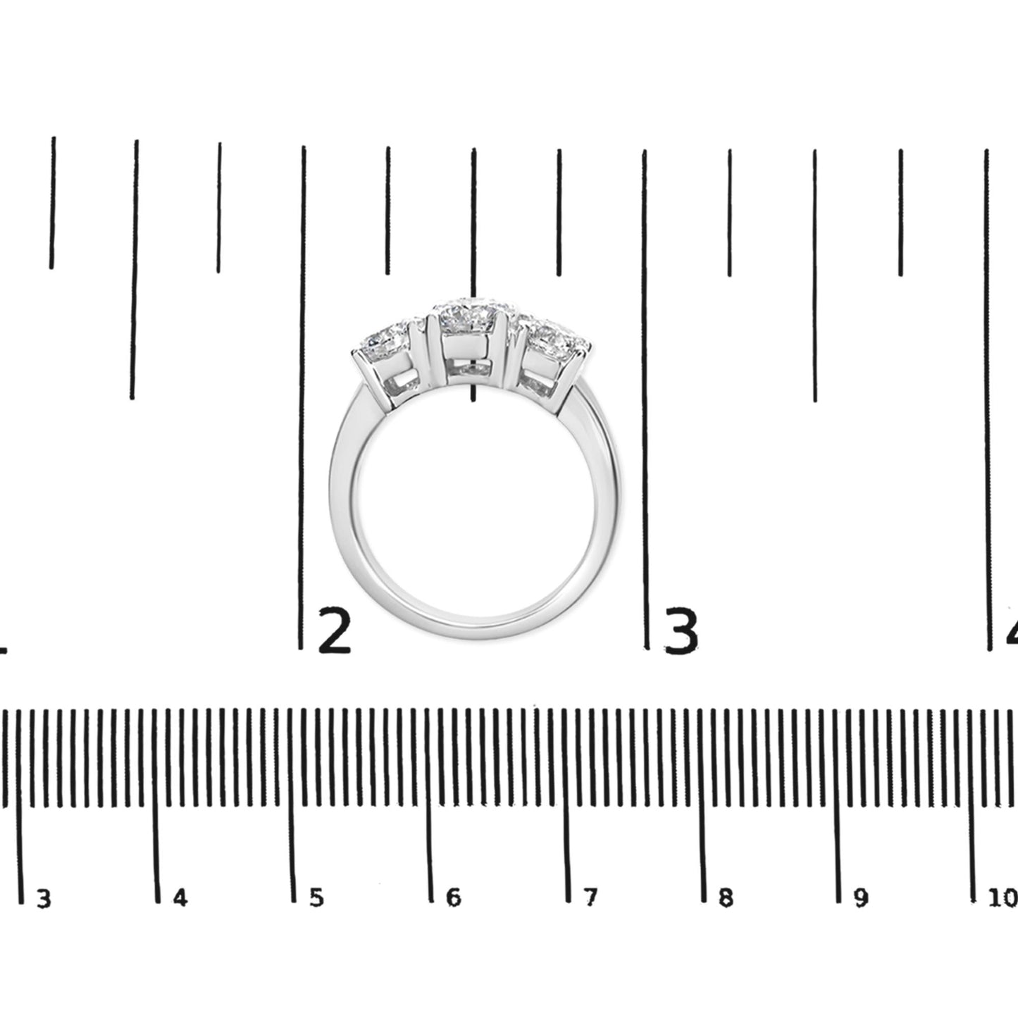 White metal ring with three round white gemstones in prong settings, shown from the top on a ruler for size reference.