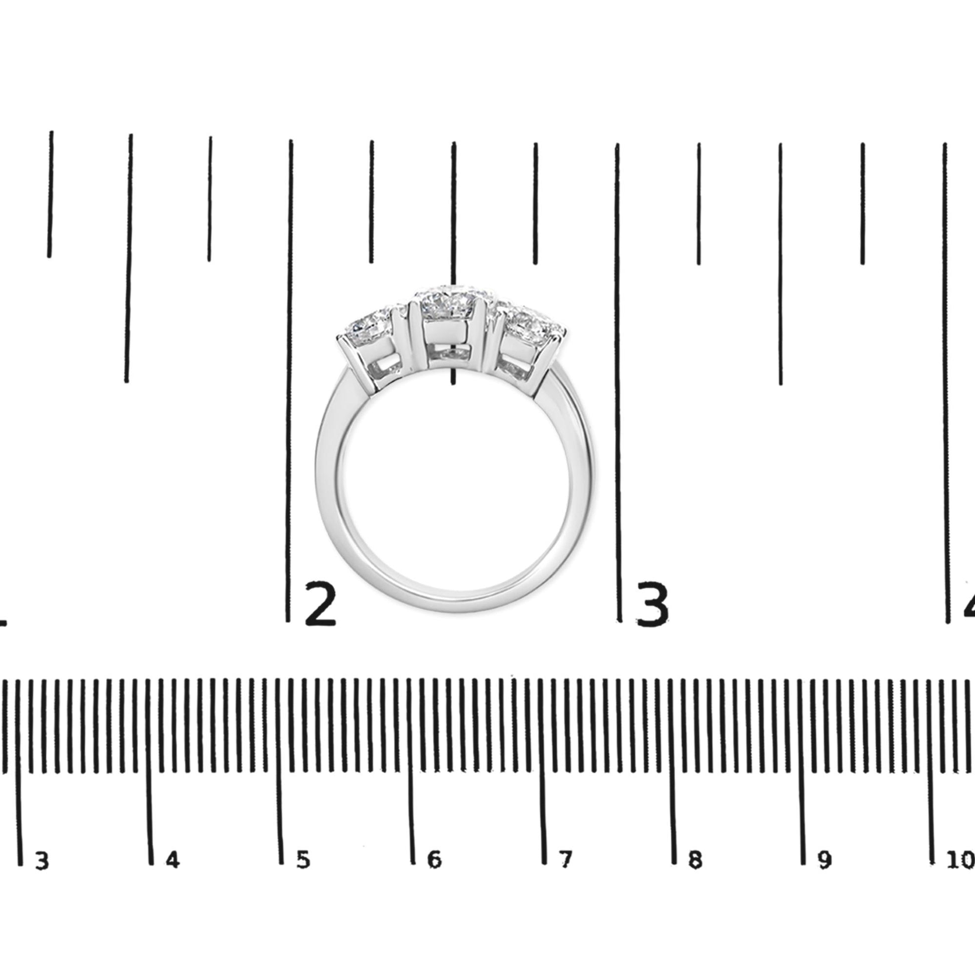 White metal ring with three round white gemstones in prong settings, shown from the top on a ruler for size reference.