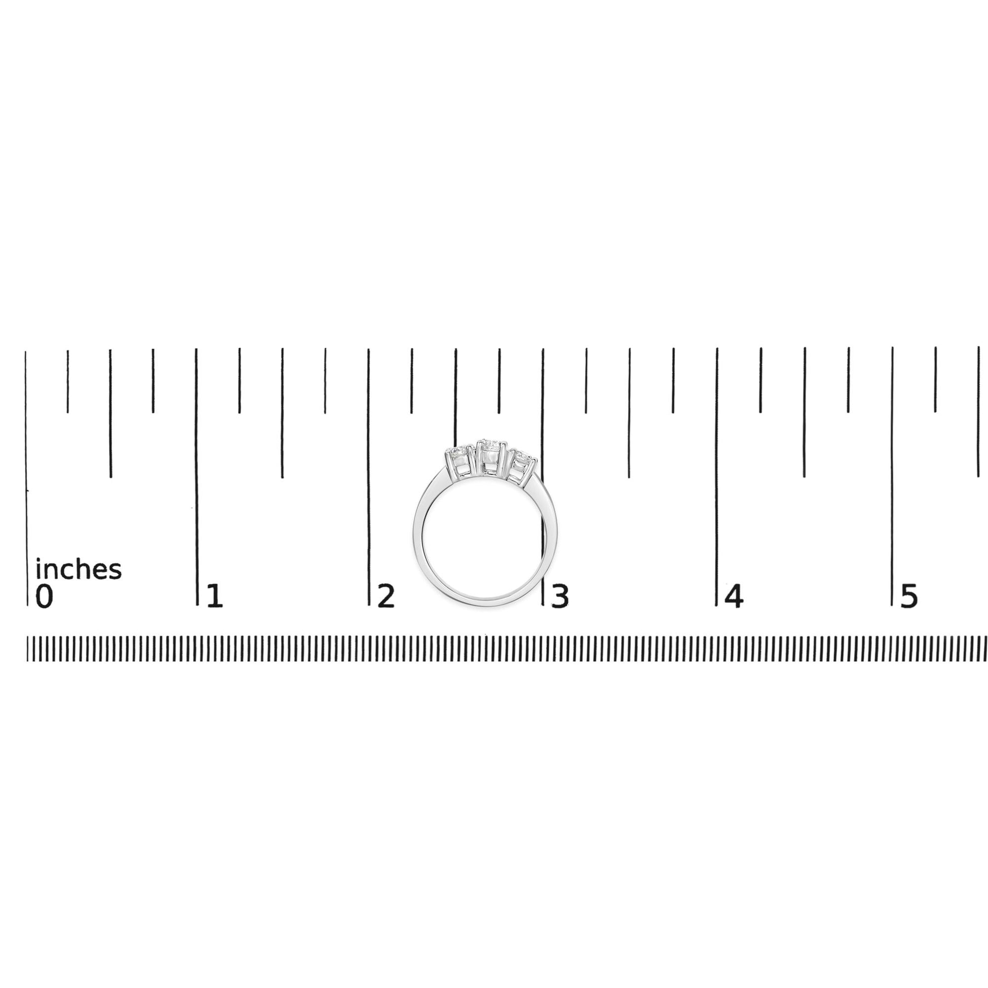 White metal ring with three round white gemstones in 4-prong settings, shown from the front on a ruler for size reference.
