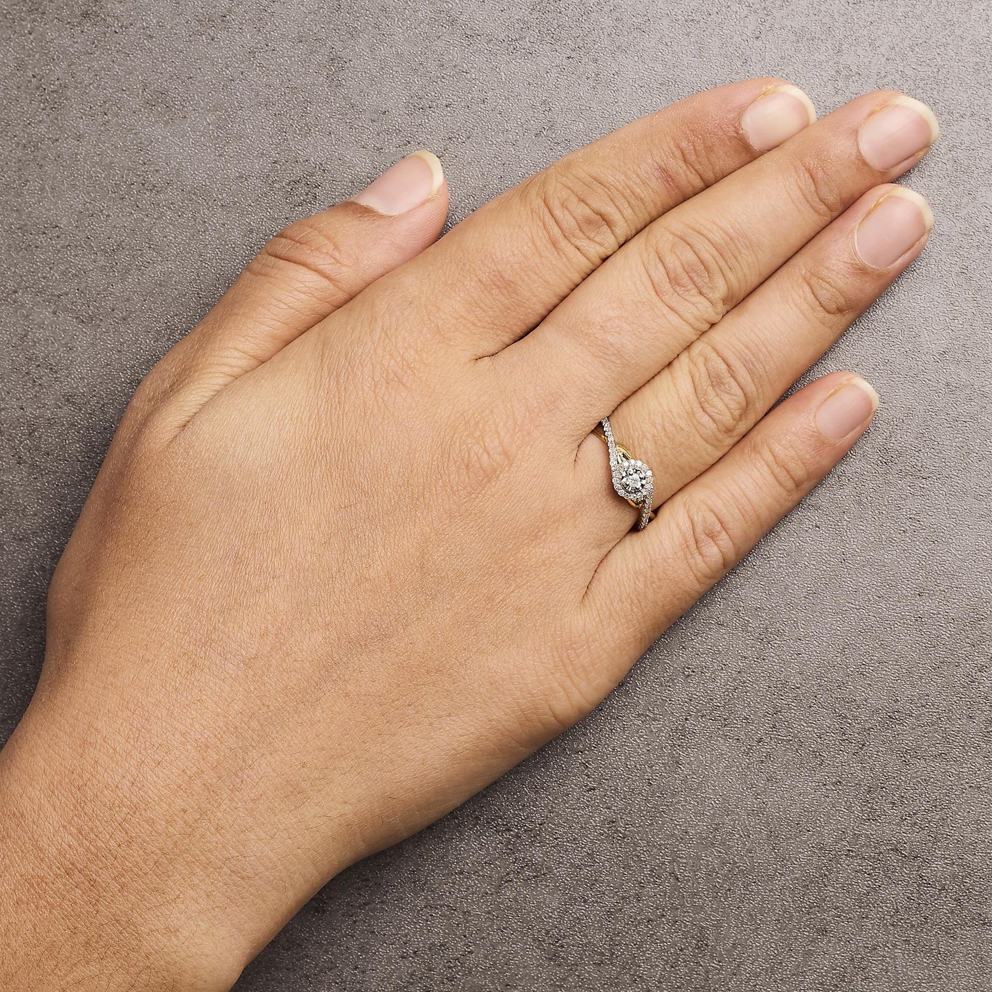 Close-up front angle of a hand wearing a yellow and white metal ring with a round white central gemstone surrounded by smaller round white gemstones.