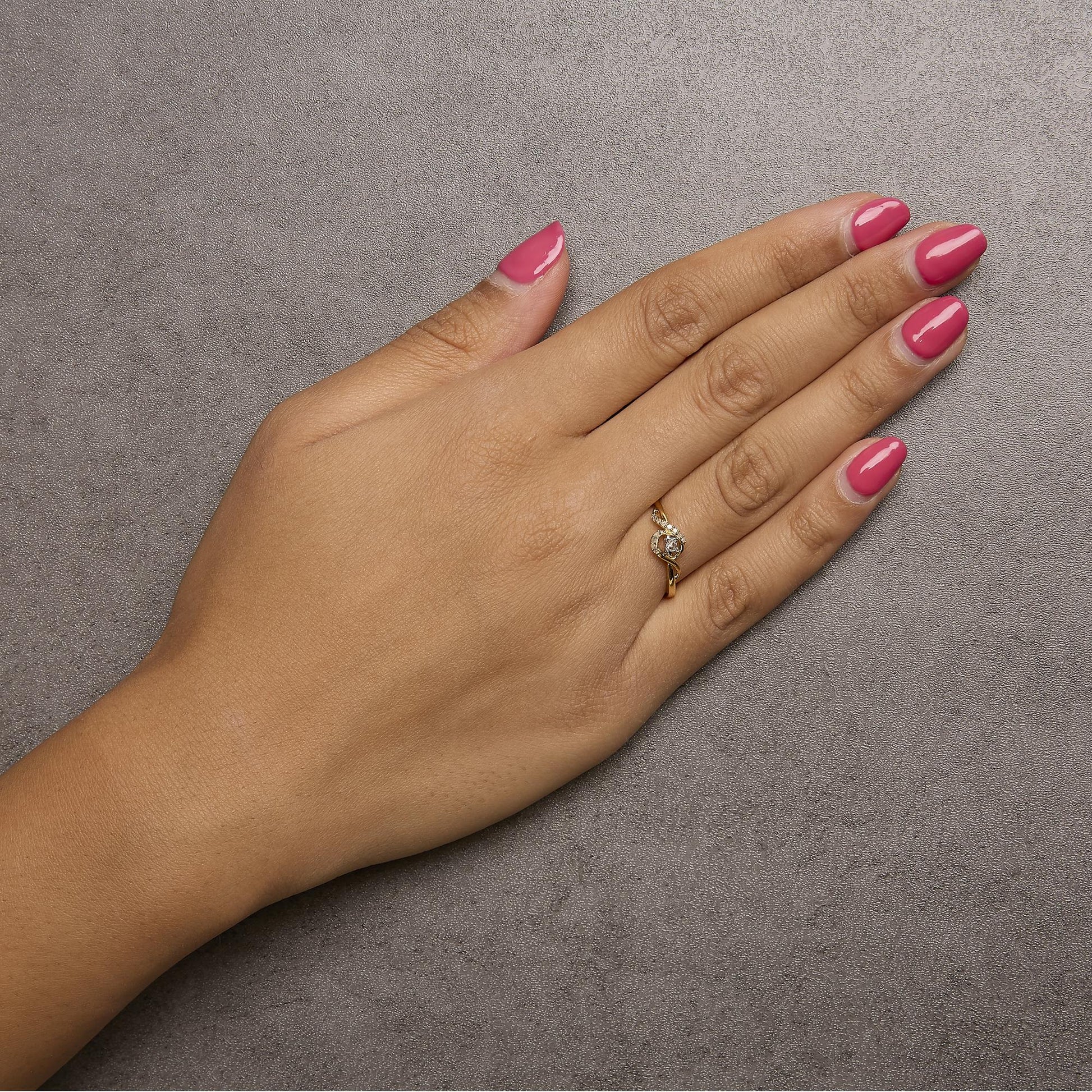 Yellow metal ring with a twisted band and a single round white gemstone in prong setting, shown worn on a model's finger from a top angle.