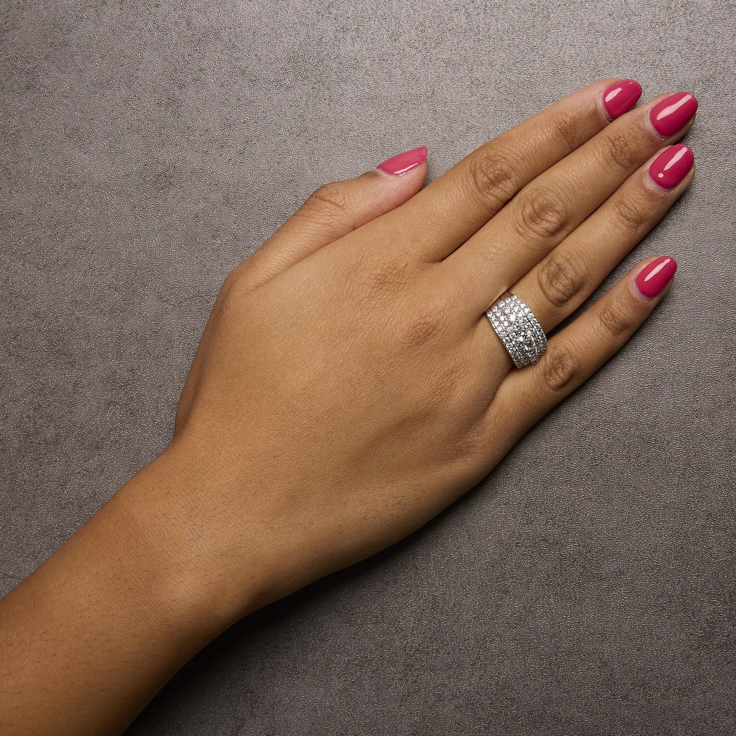 White metal wide band ring with multiple rows of round white gemstones in prong settings, shown worn on a model's finger, top angle view.