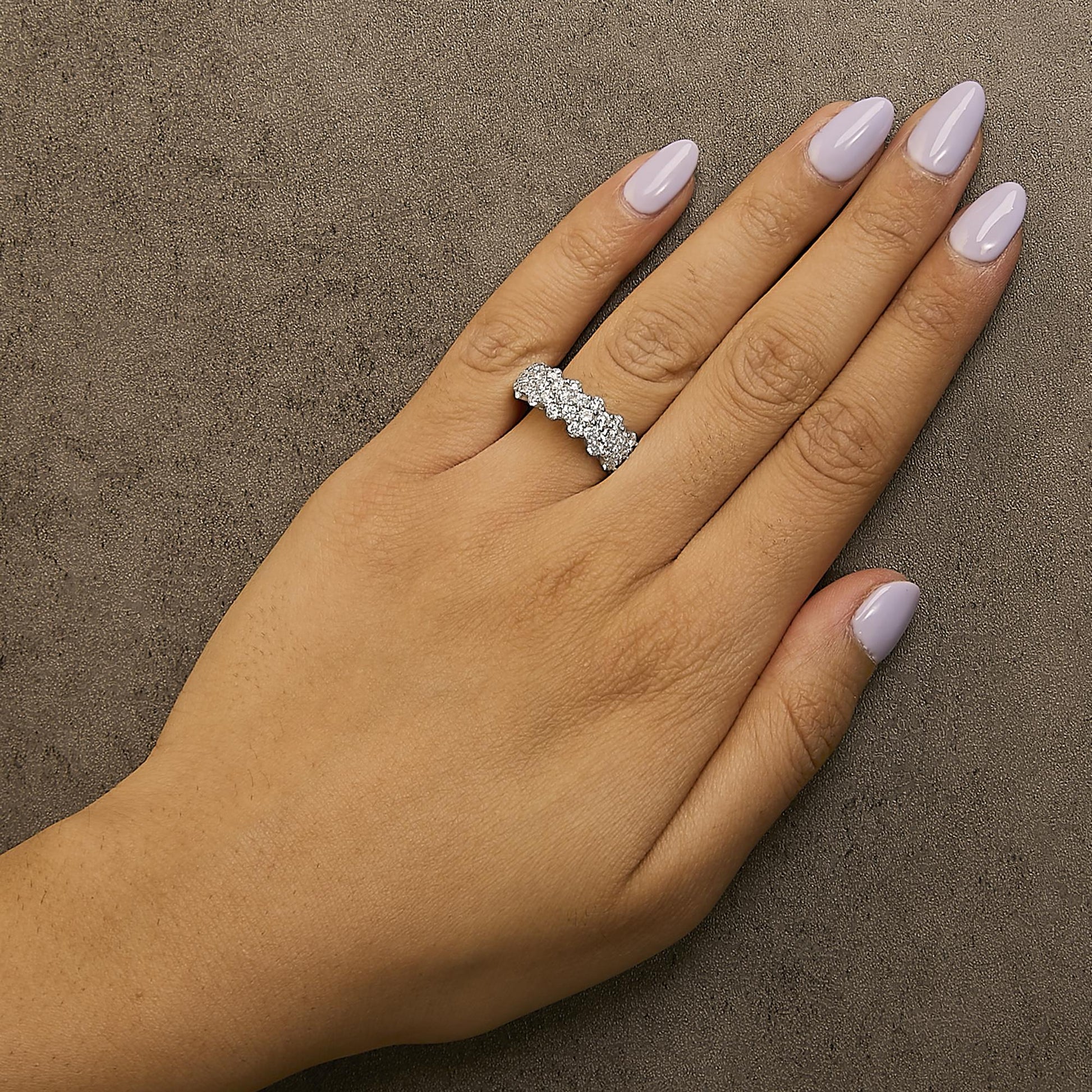 Close-up side angle of a white metal ring with two rows of round white gemstones in prong settings, worn on a model's finger.