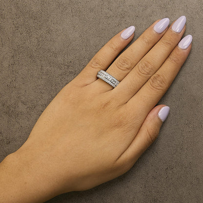 Close-up angled top view of a white metal ring with two rows of round white gemstones in prong settings, shown worn on a model's finger with lavender nail polish.