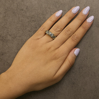 Close-up shot of a yellow metal ring with round prong-set champagne-colored gemstones arranged in a lattice pattern, shown worn on a model's finger.