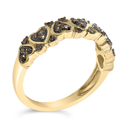 Yellow metal ring with heart-shaped designs, each featuring multiple prong-set round champagne-colored gemstones, shown at an angled close-up view.