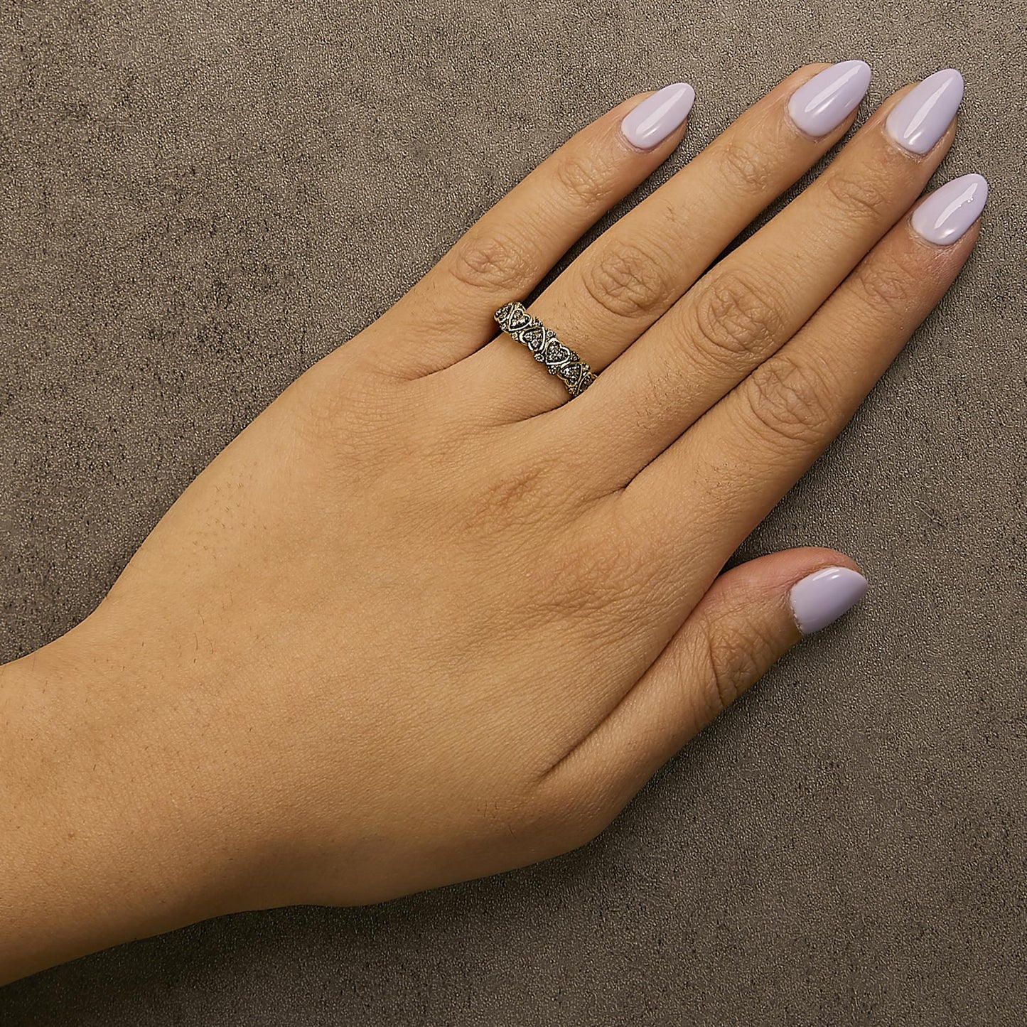 Yellow metal ring with heart-shaped design and round champagne-colored gemstones in prong settings, shown worn on a model's hand, top-down angle.