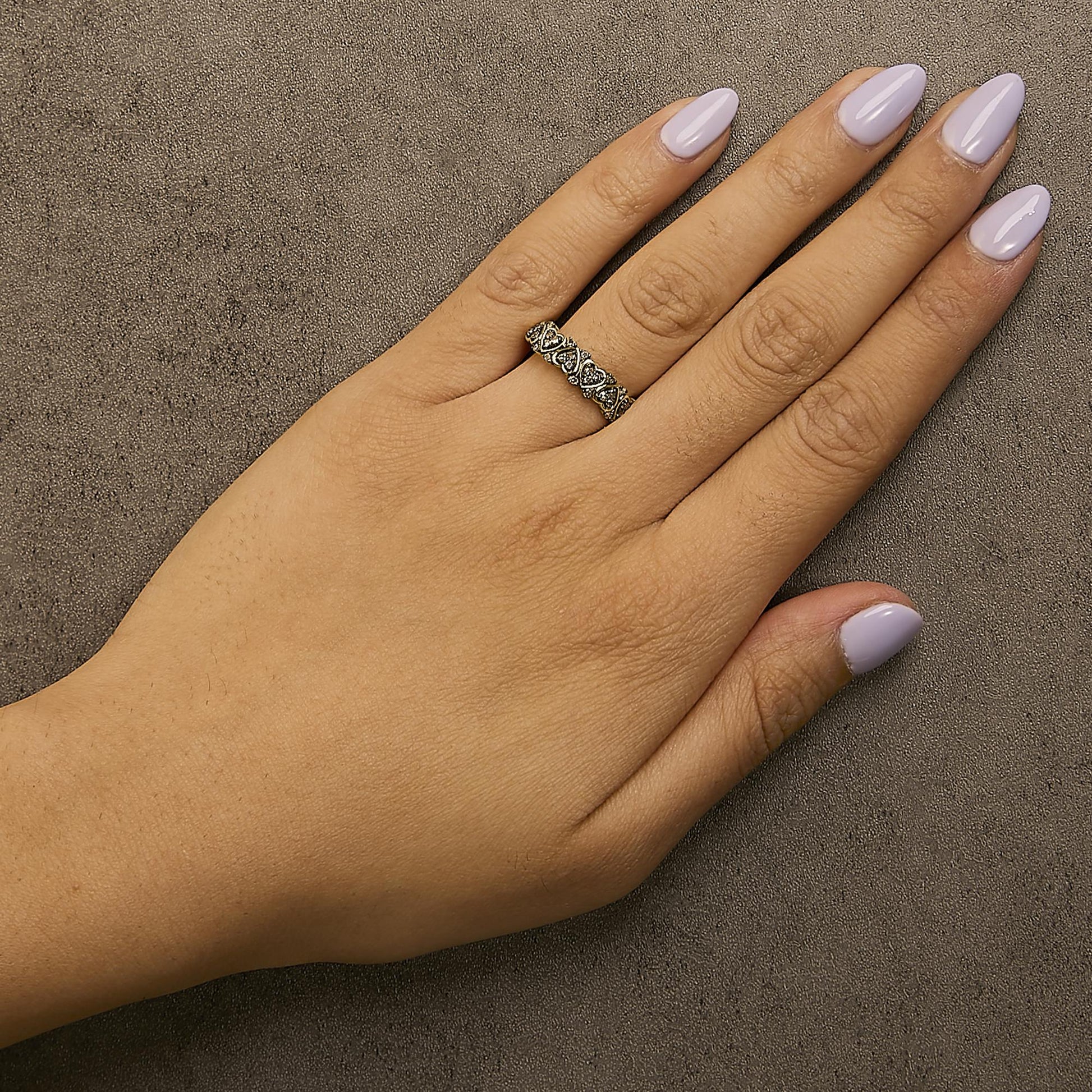 Yellow metal ring with heart-shaped design and round champagne-colored gemstones in prong settings, shown worn on a model's hand, top-down angle.