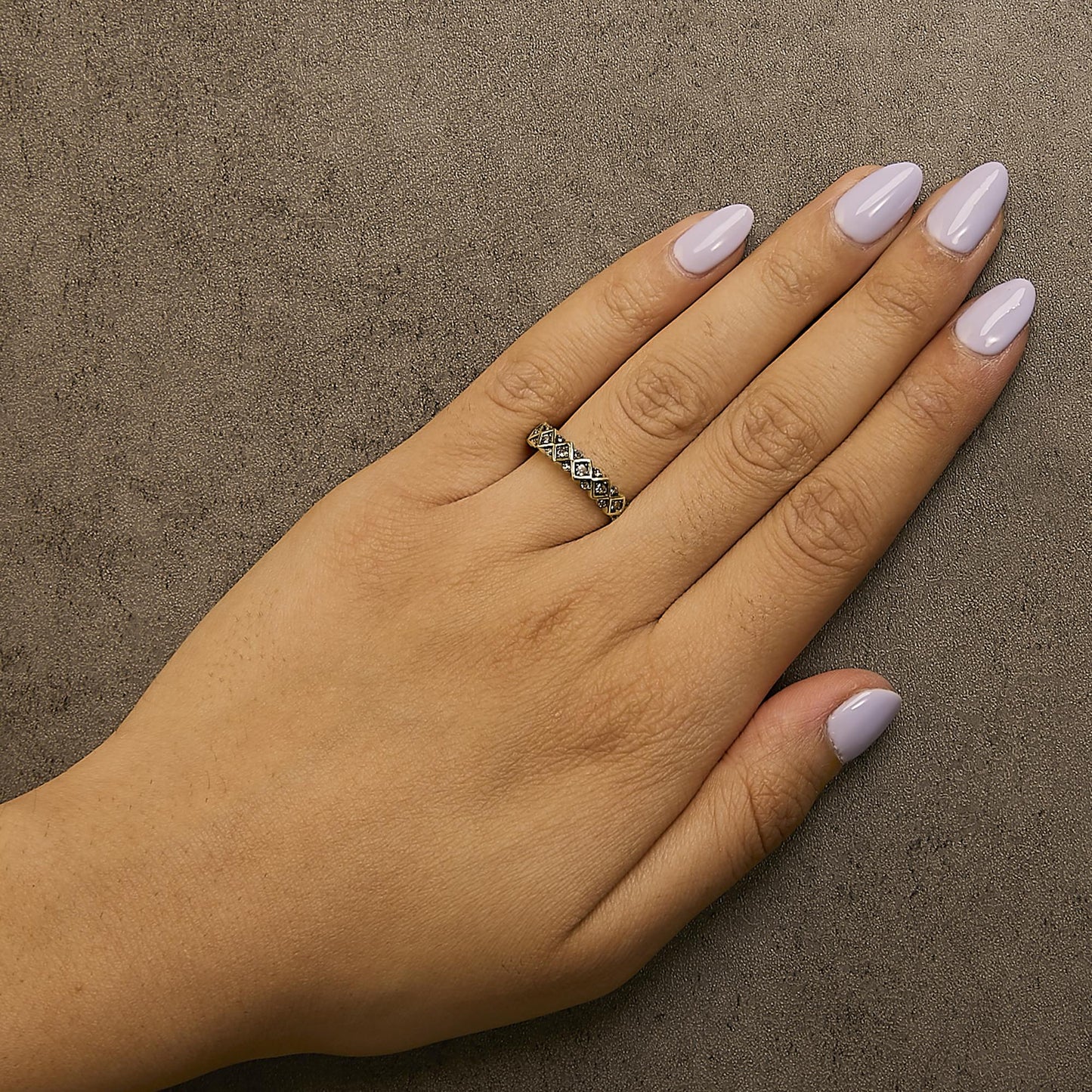 Close-up angled view of a yellow metal ring with multiple round champagne-colored gemstones in prong settings, worn on a model's finger with light purple nail polish.