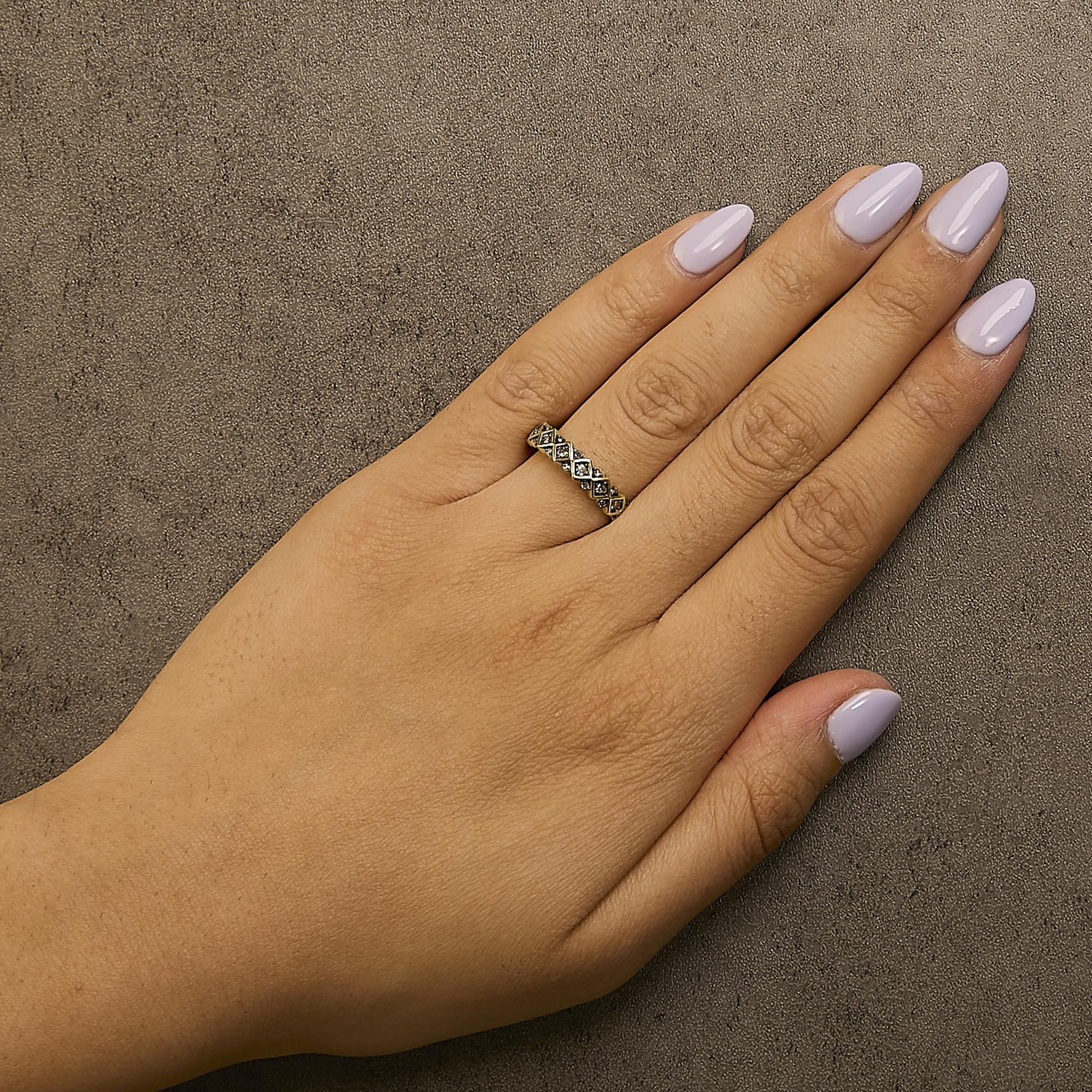 Close-up angled view of a yellow metal ring with multiple round champagne-colored gemstones in prong settings, worn on a model's finger with light purple nail polish.