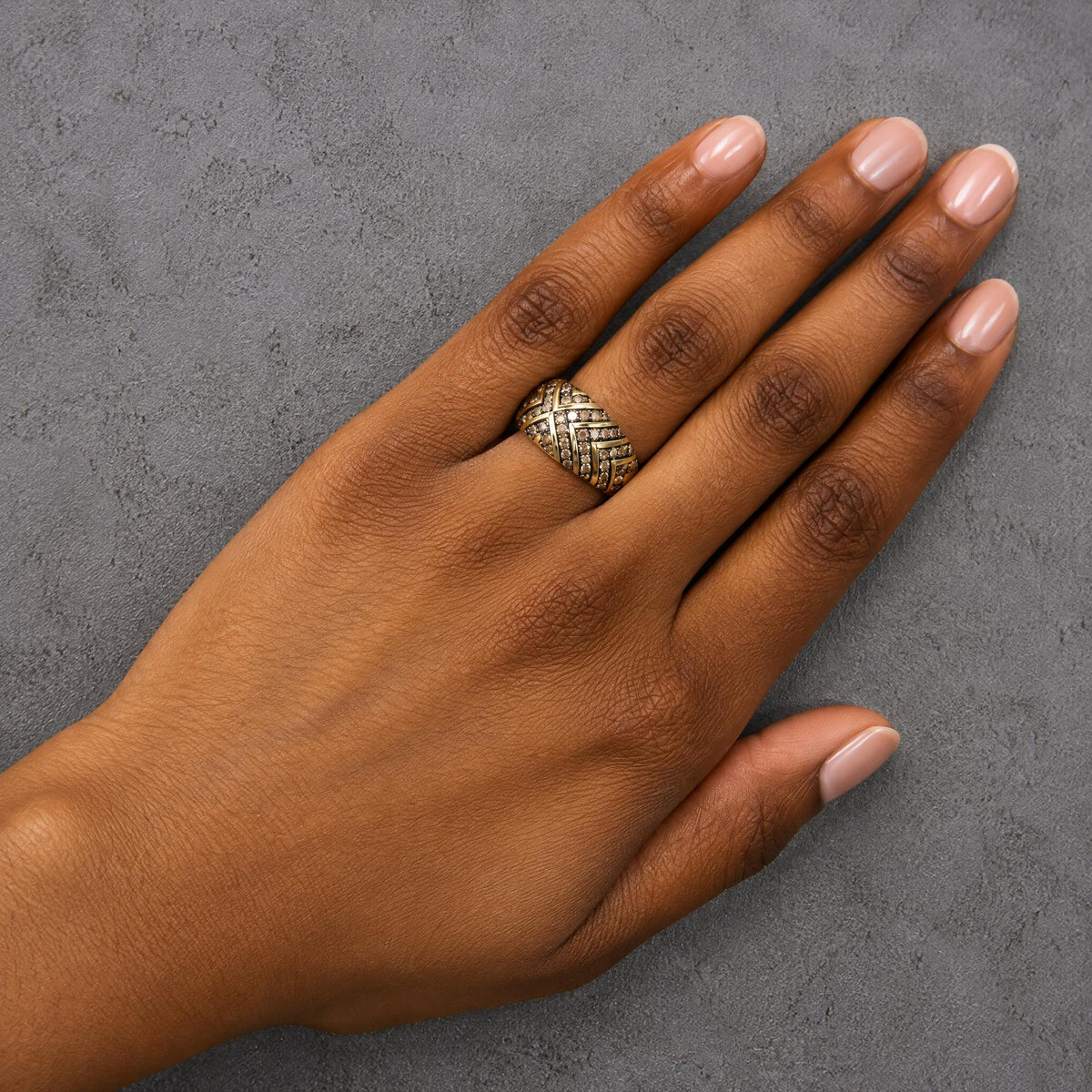 Yellow metal ring with crisscross pattern featuring round champagne-colored gemstones in prong settings, shown worn on a model’s hand from a top-down angle.