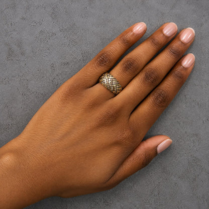 Yellow metal ring with crisscross pattern featuring round champagne-colored gemstones in prong settings, shown worn on a model’s hand from a top-down angle.