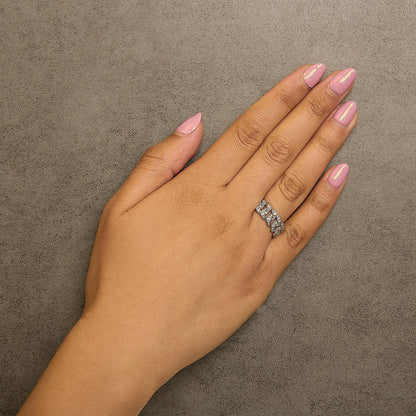 Yellow metal ring with round white gemstones in prong settings arranged in a linked chain pattern, shown worn on a model's finger, angled from above.
