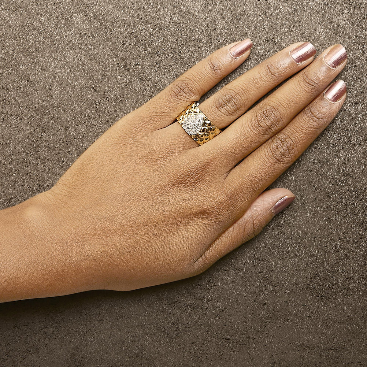 Yellow ring with a wide textured band and a heart-shaped cluster of white gemstones in prong setting, shown worn on a model's finger from a top angle.