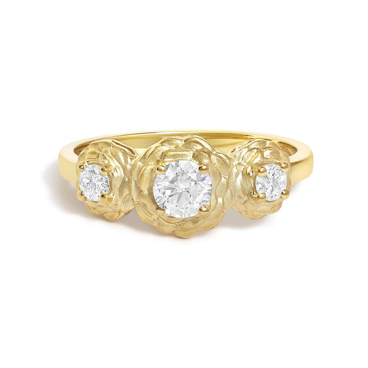 Close-up image of a yellow metal ring with three round white gemstones set in prongs, the center gemstone is larger, surrounded by a textured floral design, shown from the front angle.
