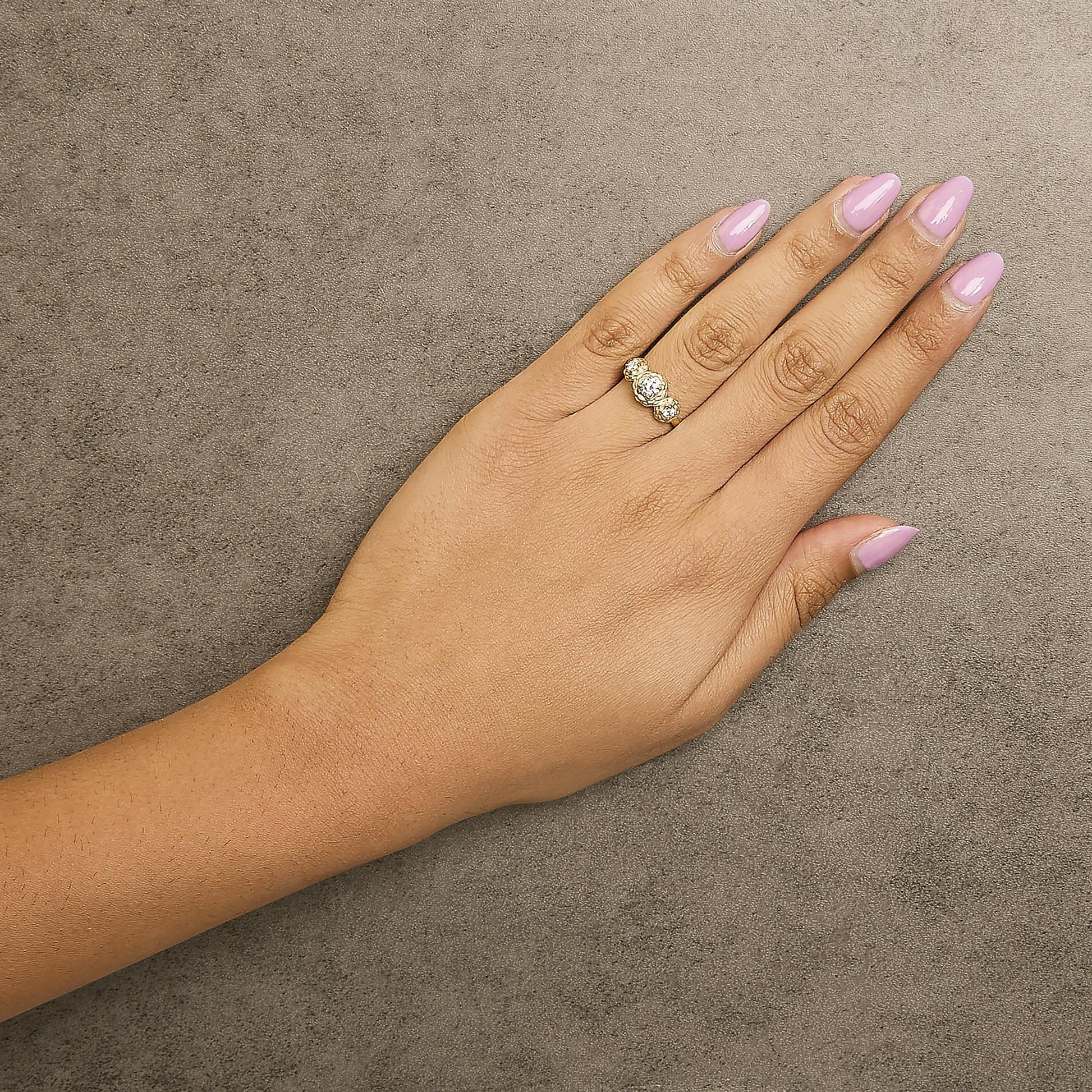 Yellow ring with three round white gemstones in prong settings, shown worn on a model’s hand viewed from above.