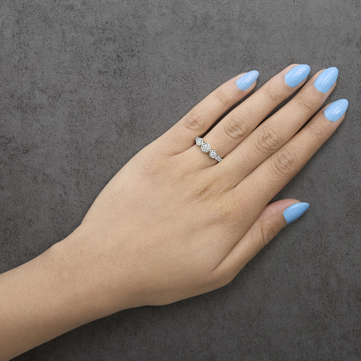 Yellow metal ring with five white round gemstones in prong and bezel settings, shown worn on a model's hand in a top-down view.