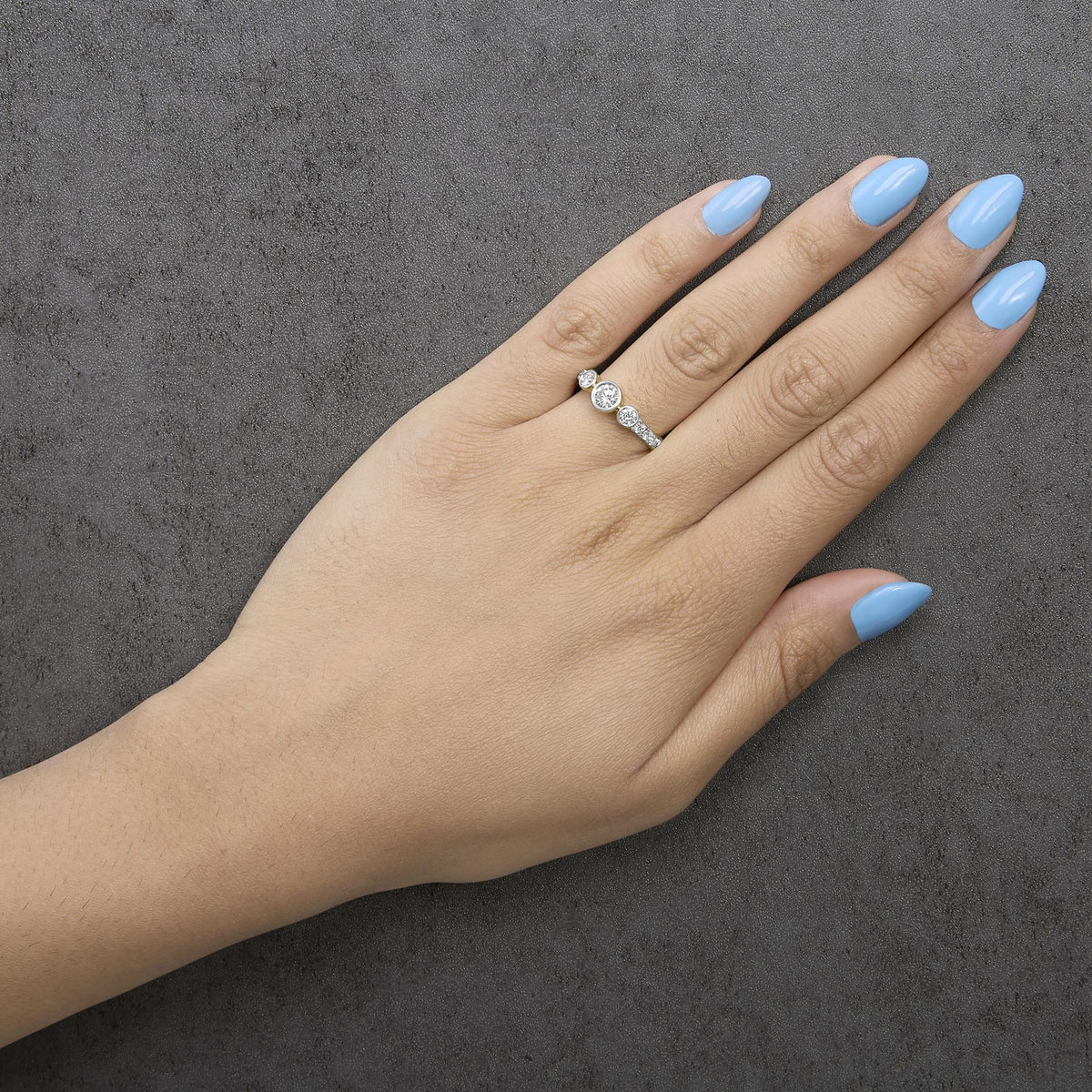 Yellow metal ring with round white gemstones in bezel and prong settings, shown worn on a model's finger, photographed from above at an angle.