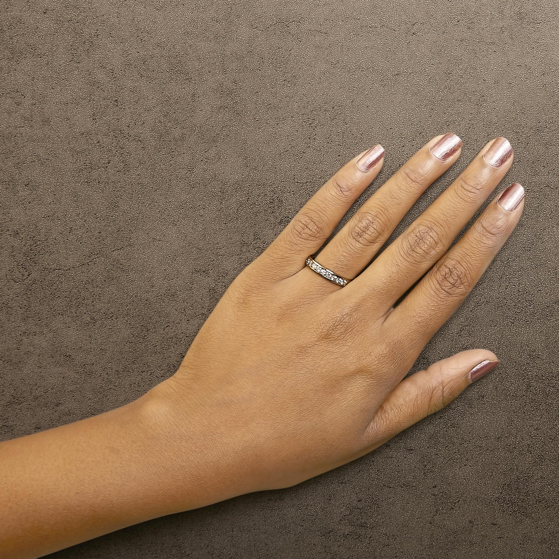 Yellow ring with white round gemstones in channel setting, shown worn on a model's hand, angled top view.