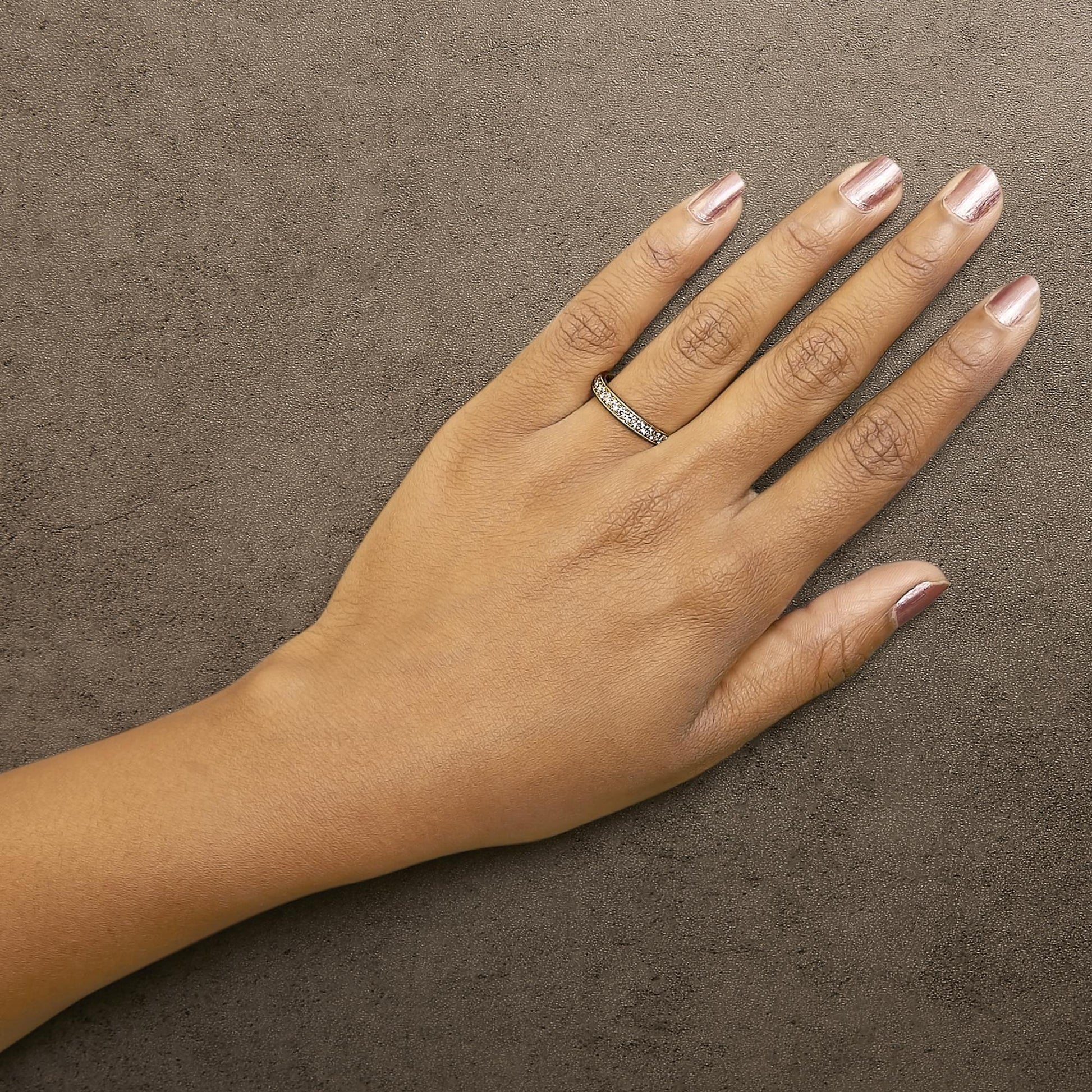 Yellow metal ring with white round gemstones in micro-pave setting, worn on a model's finger, top-down angle.