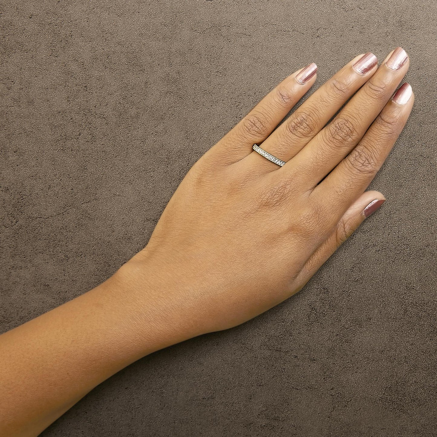 Yellow metal ring with micro-pave round white gemstones, worn on a model's finger, shown from above.