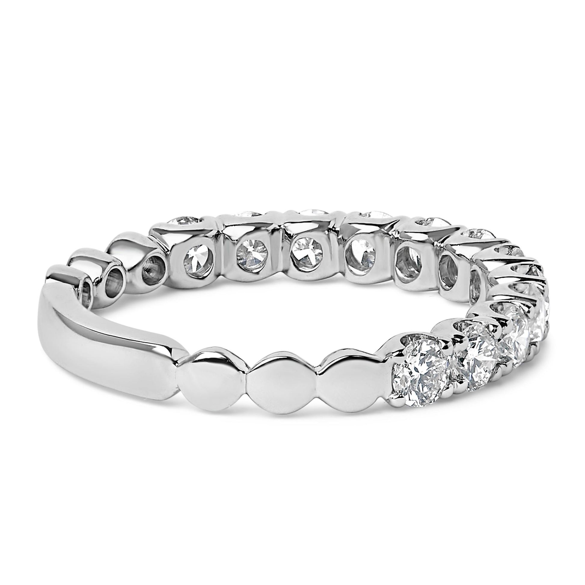 Close-up angled view of a white metal ring featuring multiple round white gemstones in 4-prong settings encircling the band.