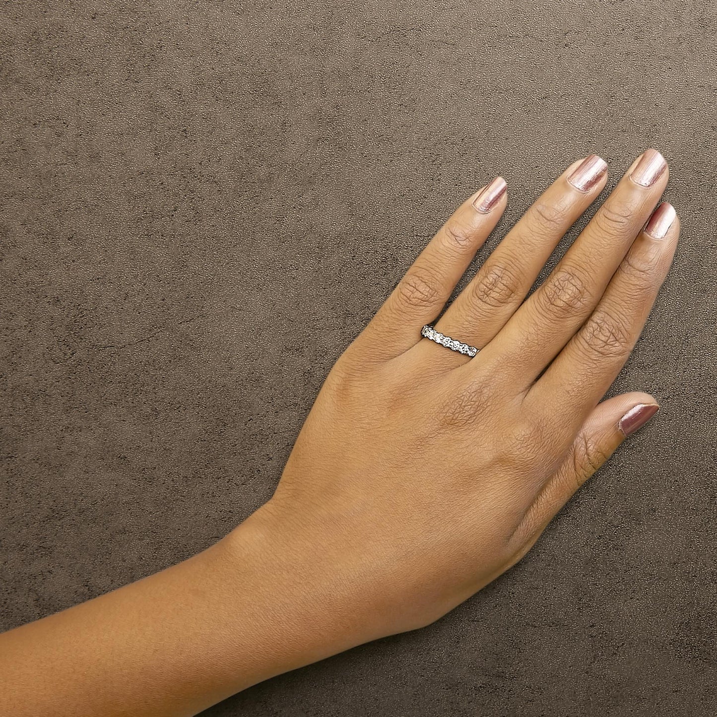 White metal ring with a row of round white gemstones in 4-prong settings, shown worn on a model's hand, top-down angle.