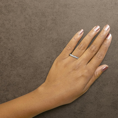 White metal ring with a row of round white gemstones in 4-prong settings, shown worn on a model's hand, top-down angle.