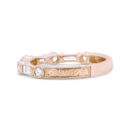 Close-up side angle of a rose-colored ring featuring round white gemstones in bezel settings and baguette white gemstones in an invisible setting, with engraved detailing.