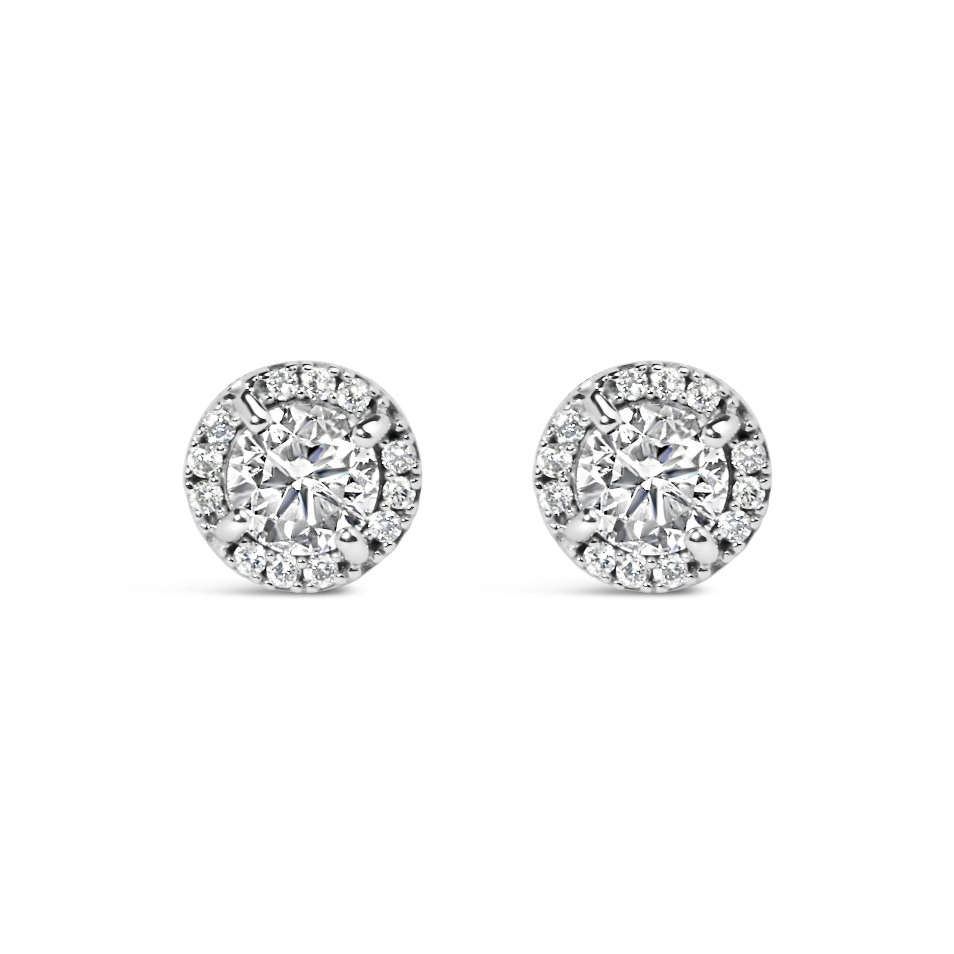 Front view of a pair of white metal stud earrings featuring a central round gemstone in a four-prong setting, surrounded by smaller round gemstones in a shared prong and channel setting.