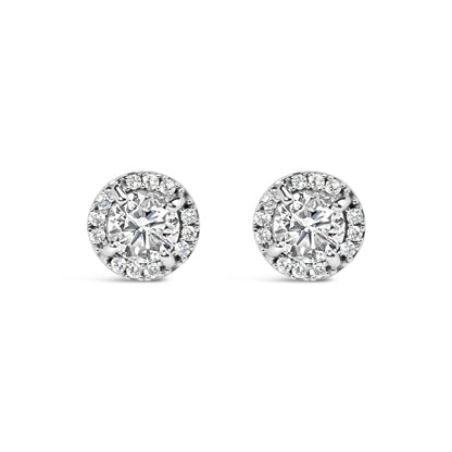 Front view of a pair of white metal stud earrings featuring a central round gemstone in a four-prong setting, surrounded by smaller round gemstones in a shared prong and channel setting.