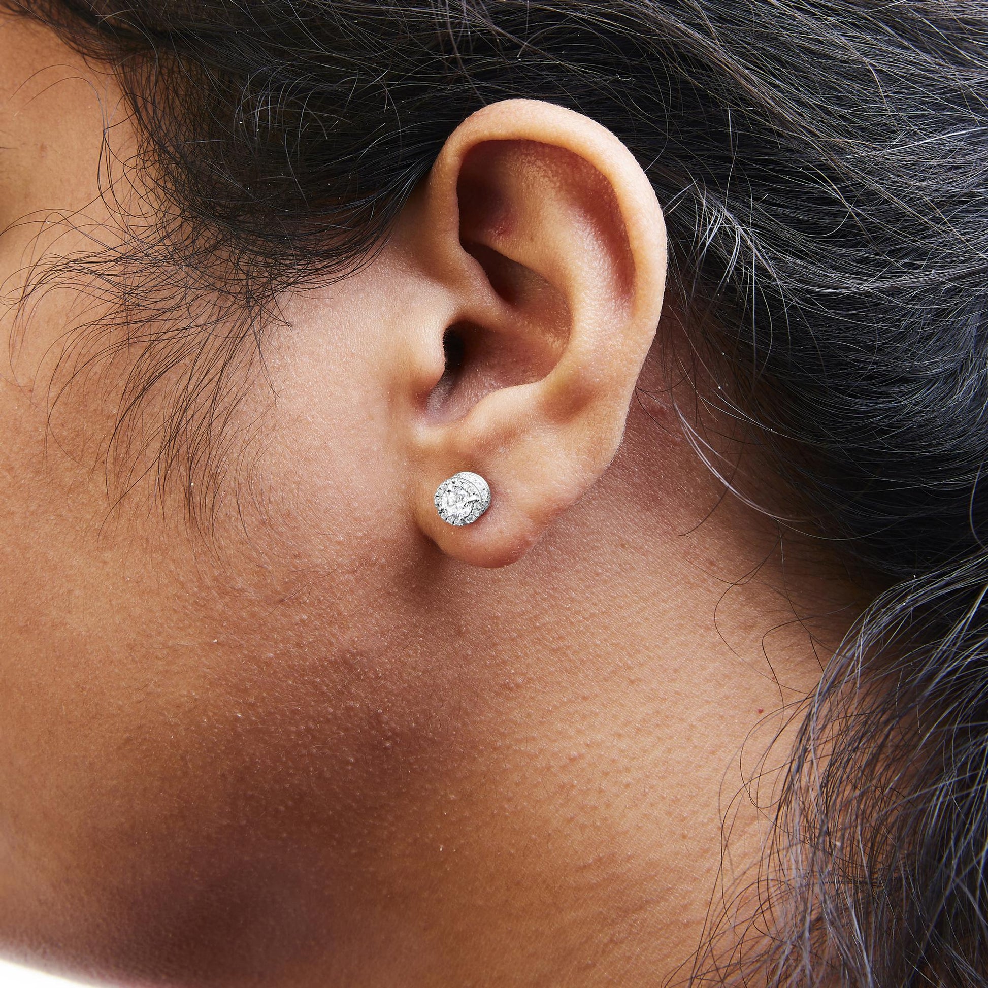 Close-up side view of a white metal stud earring with round white gemstones in 4-prong, shared prong, and channel settings worn on a model's ear.
