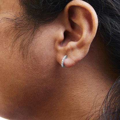 Close-up side view of a white metal hoop earring adorned with multiple round white gemstones in 4-prong settings, worn on a model's ear.
