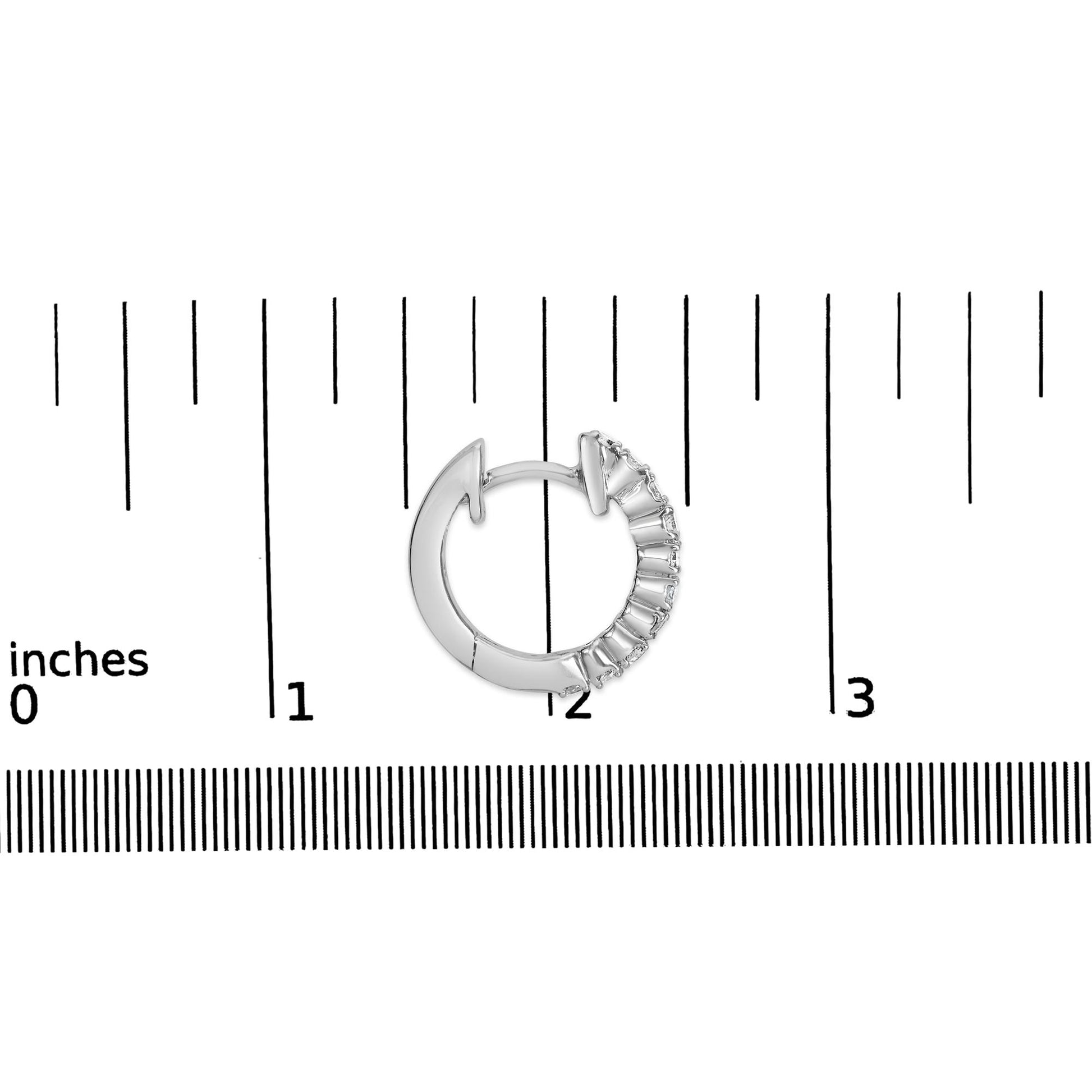 Close-up top view of a white metal hoop earring set with round white gemstones in 4-prong settings, placed on a ruler for size reference.