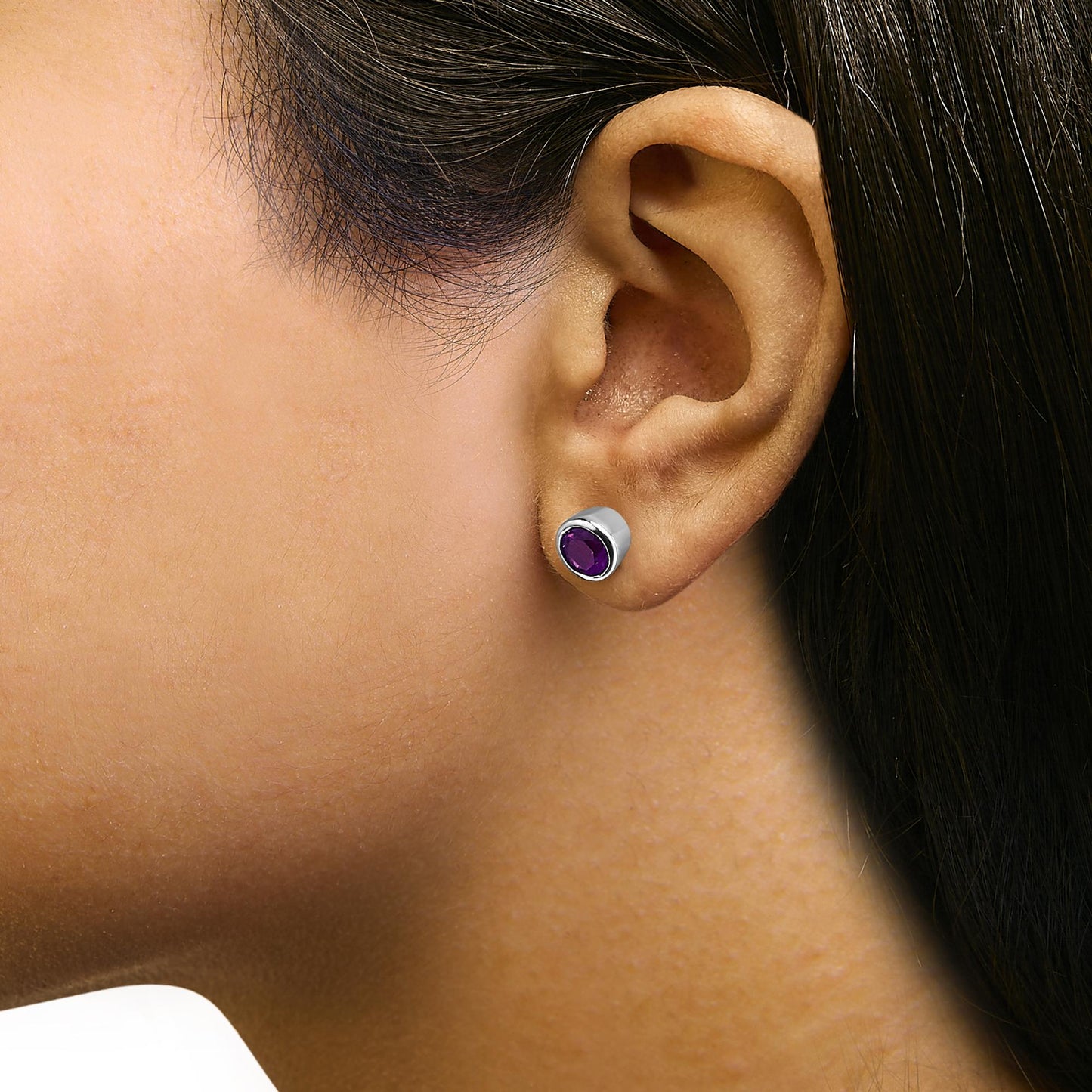 Close-up side view of a model wearing round purple gemstone stud earrings in a white metal bezel setting.