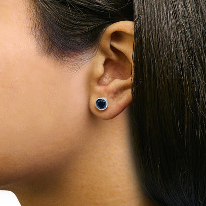 Close-up side view of white metal stud earring with round blue gemstones set in a bezel setting, worn on a model.