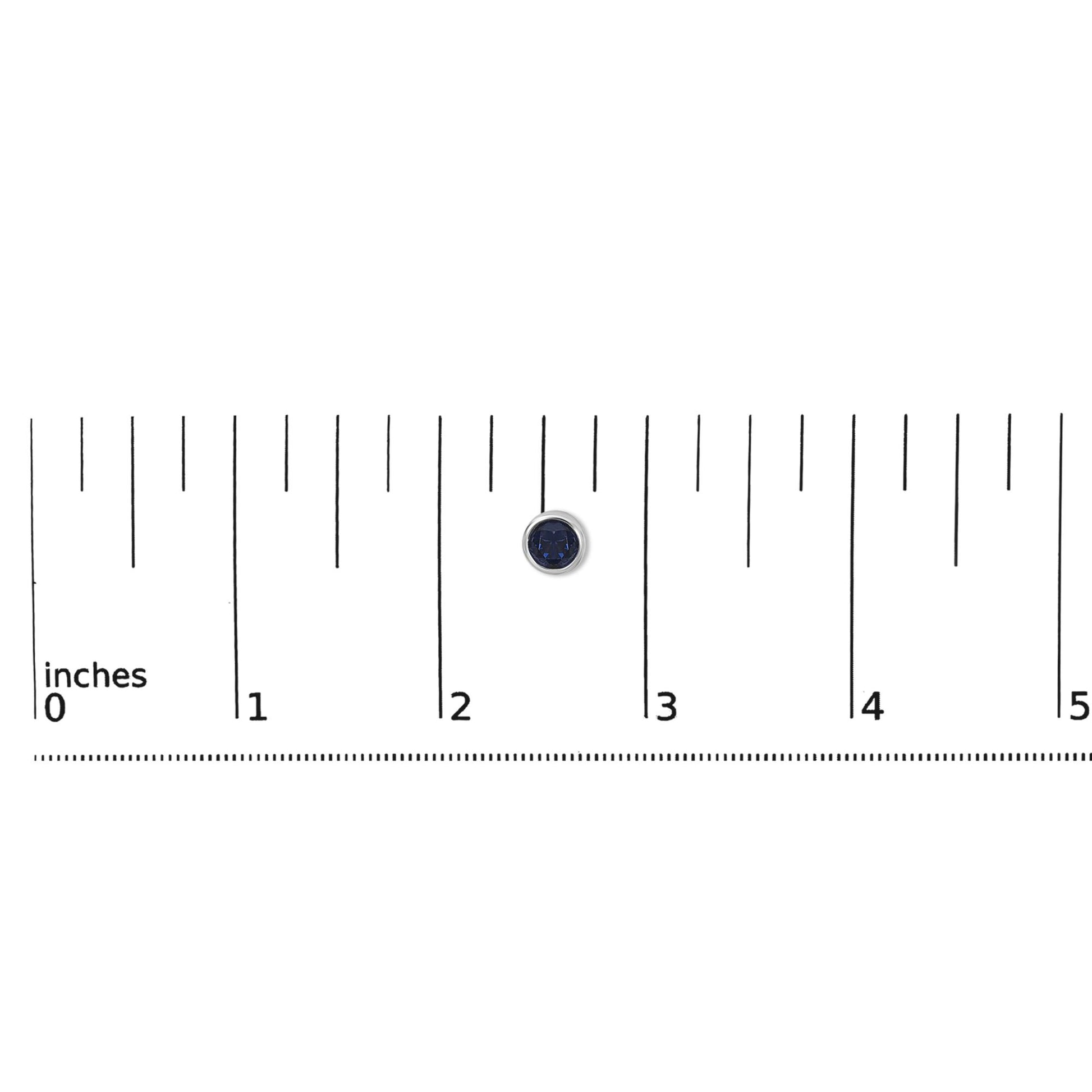 Close-up of a single round blue gemstone earring with a white metal bezel setting, shown flat on a ruler for scale.