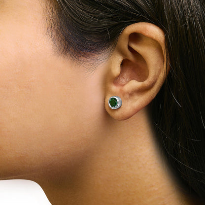 Close-up side view of a model wearing a pair of white metal stud earrings featuring round green gemstones in bezel settings.