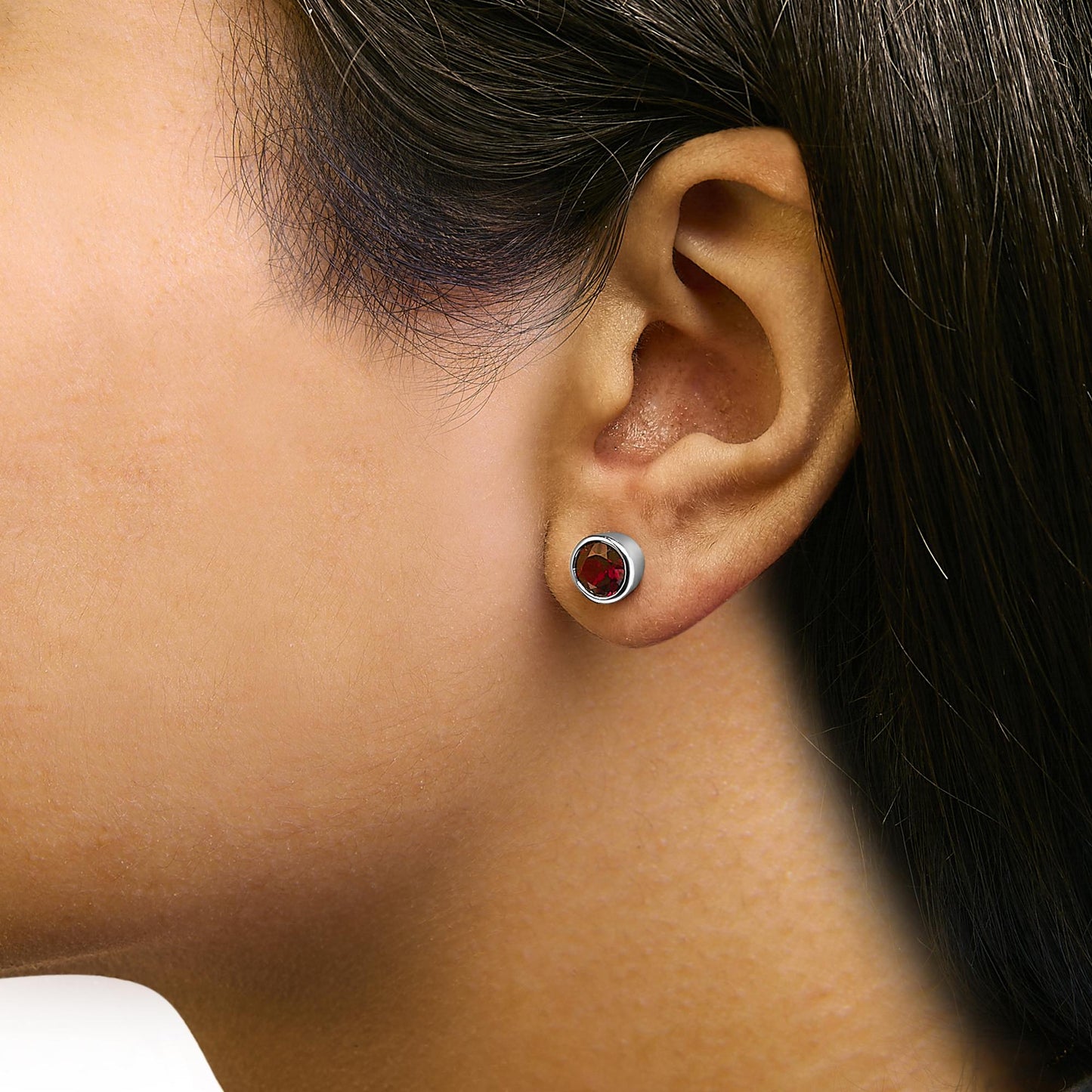 Close-up side view of a model wearing white metal stud earrings with round red gemstones in bezel settings.