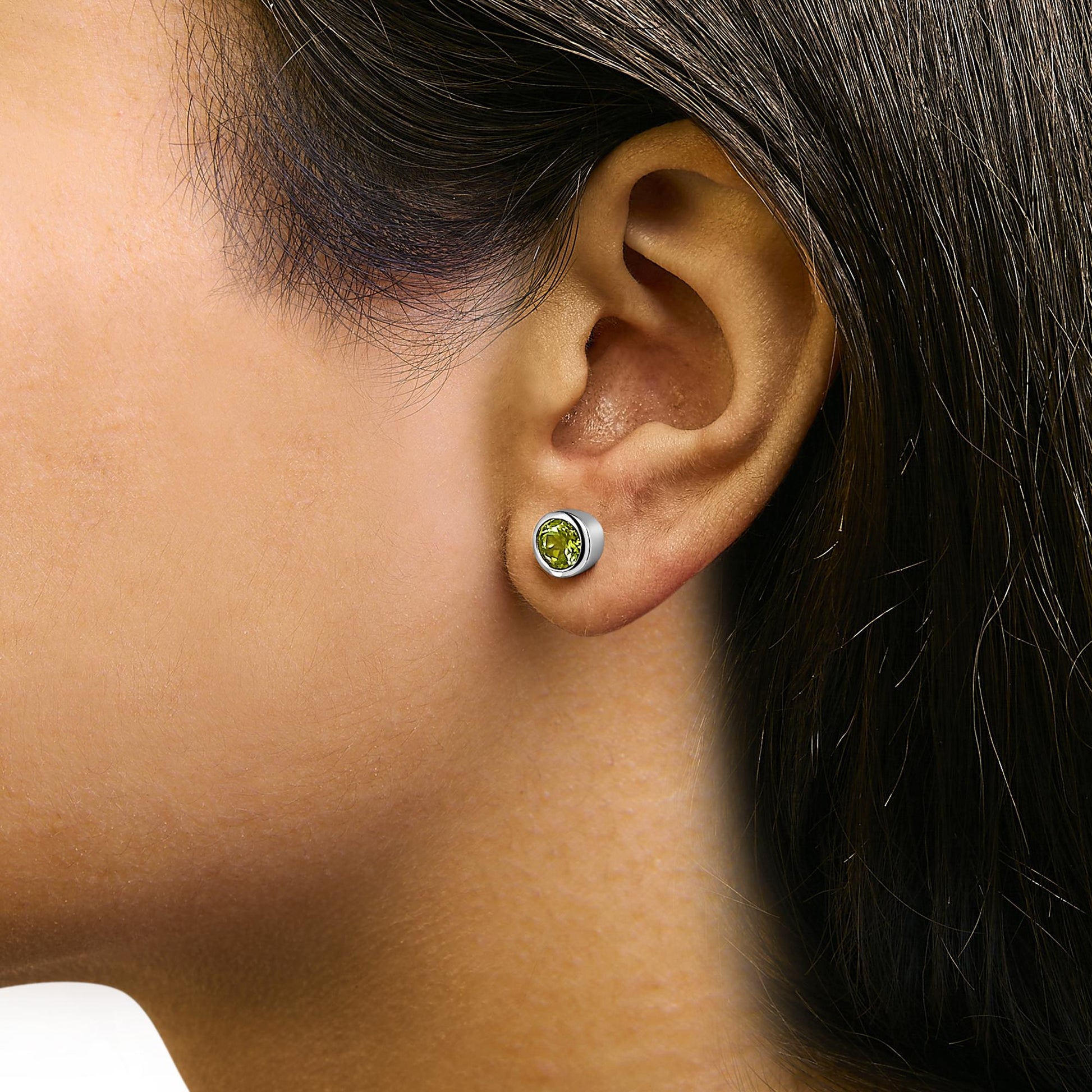 Close-up side view of a model wearing white metal stud earrings with round green gemstones in bezel settings.