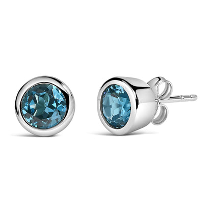 Pair of white metal stud earrings with round blue gemstones in bezel settings, shown from a side and front angle on a white background.