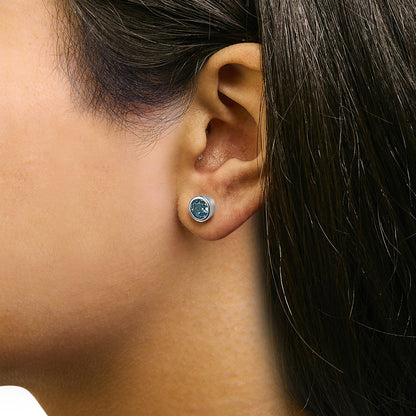 Close-up side view of a model wearing a white metal stud earring with a round blue gemstone in a bezel setting.