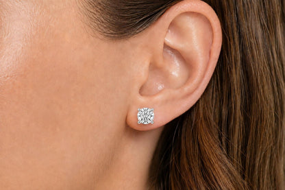 Close-up side view of a model wearing a pair of white metal stud earrings, each featuring a round white gemstone in a four-prong setting.