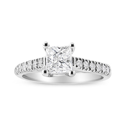 Front angled view of a white ring featuring a princess-shaped white gemstone in a four-prong setting, flanked by multiple round white gemstones along the band.