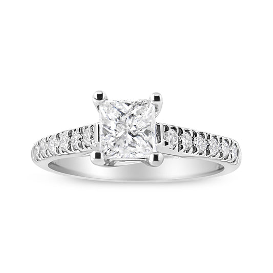 Front angled view of a white ring featuring a princess-shaped white gemstone in a four-prong setting, flanked by multiple round white gemstones along the band.