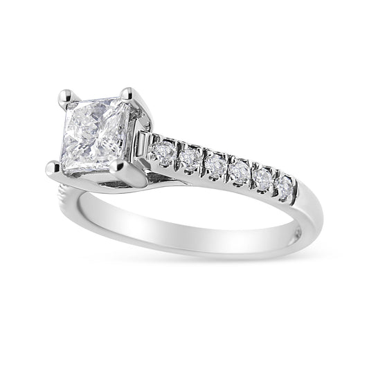 White metal ring with a princess shape white gemstone in a four-prong setting, accompanied by round white gemstones set along the band, shown in a close-up angled view.