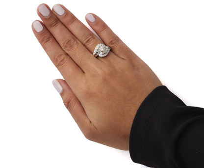 White metal ring with intertwined design featuring round prong-set white gemstones and baguette channel-set white gemstones, worn on a model's hand shown from top angle.