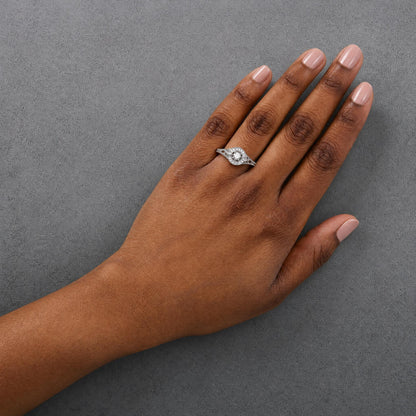 White metal ring with a round white gemstone in prong setting surrounded by smaller round white gemstones in prong settings, shown worn on a model's finger, top-down angle.